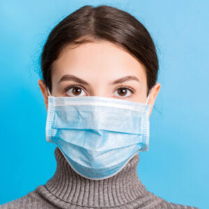 Portrait of young woman wearing medical mask at blue background. Protect your health. Coronavirus concept.